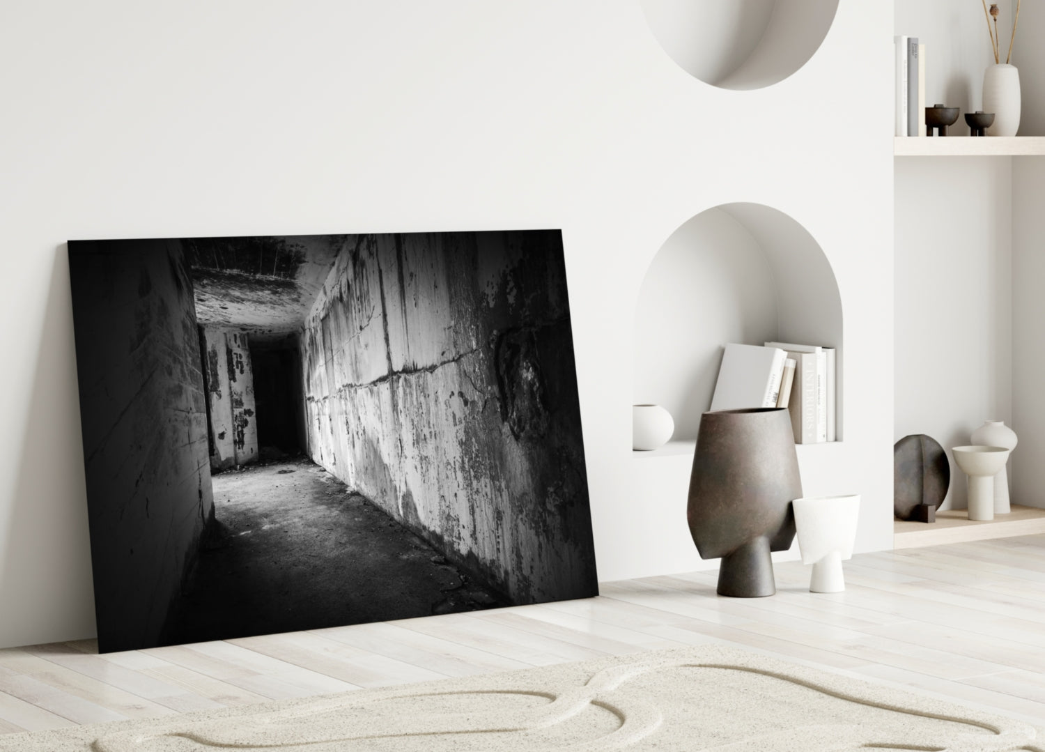 Black and white photograph of deteriorating concrete hallway with peeling walls displayed as glass wall art leaning against white wall.