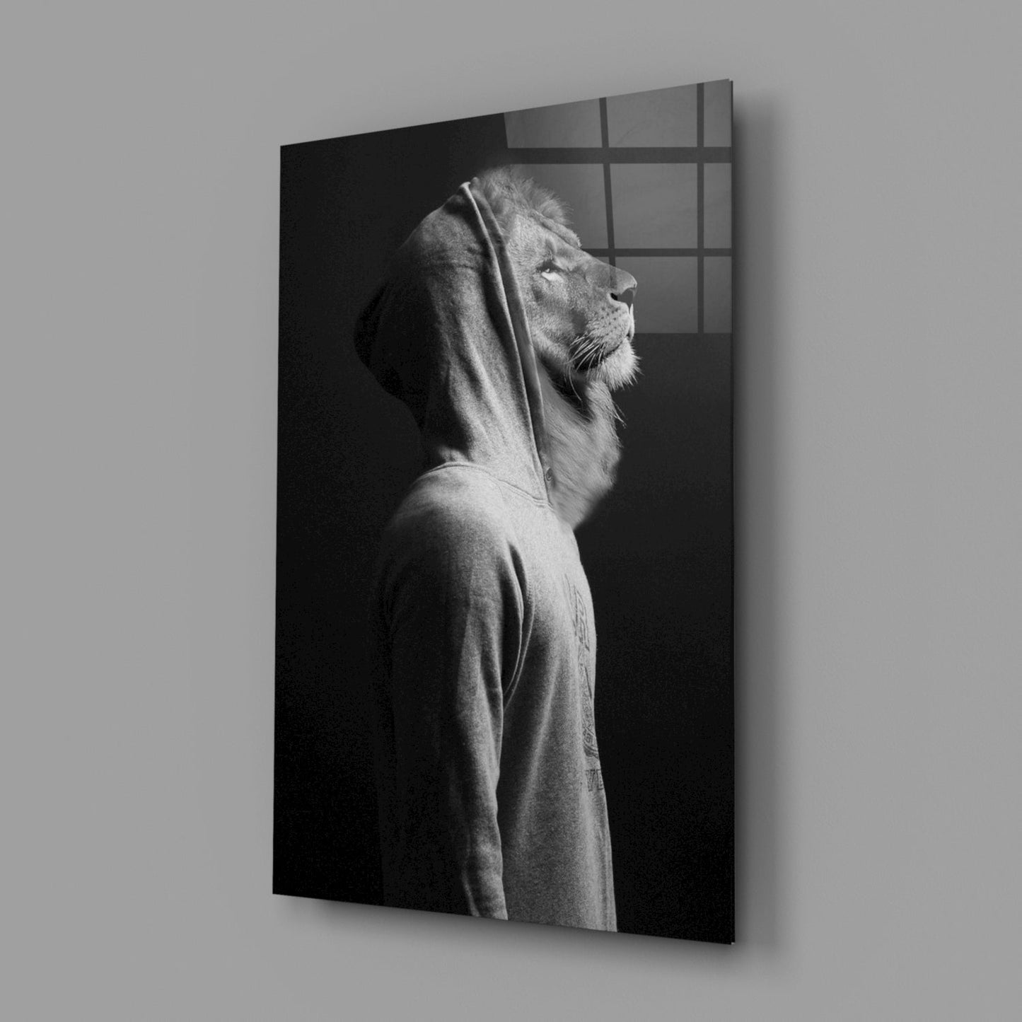 Black and white glass wall art displaying a lion's head in profile wearing a hoodie, mounted at an angle against gray wall.