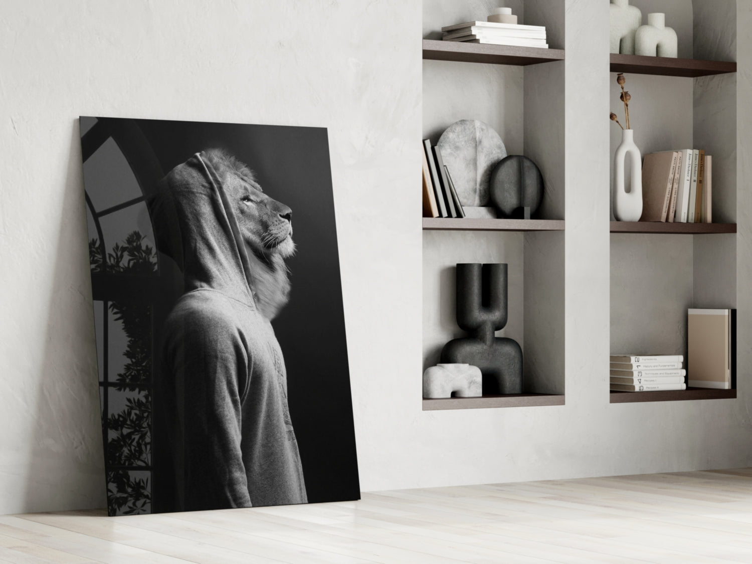 Black and white glass wall art leaning against white wall displays lion's head in profile with hooded figure, styled interior setting with wooden shelves and decorative objects.