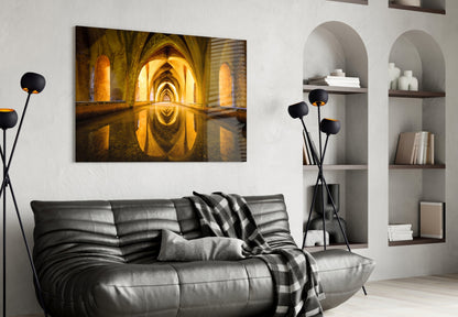 Cistern Glass Wall Art displaying illuminated golden arched tunnel with water reflection, hung above black leather sofa in modern living room.