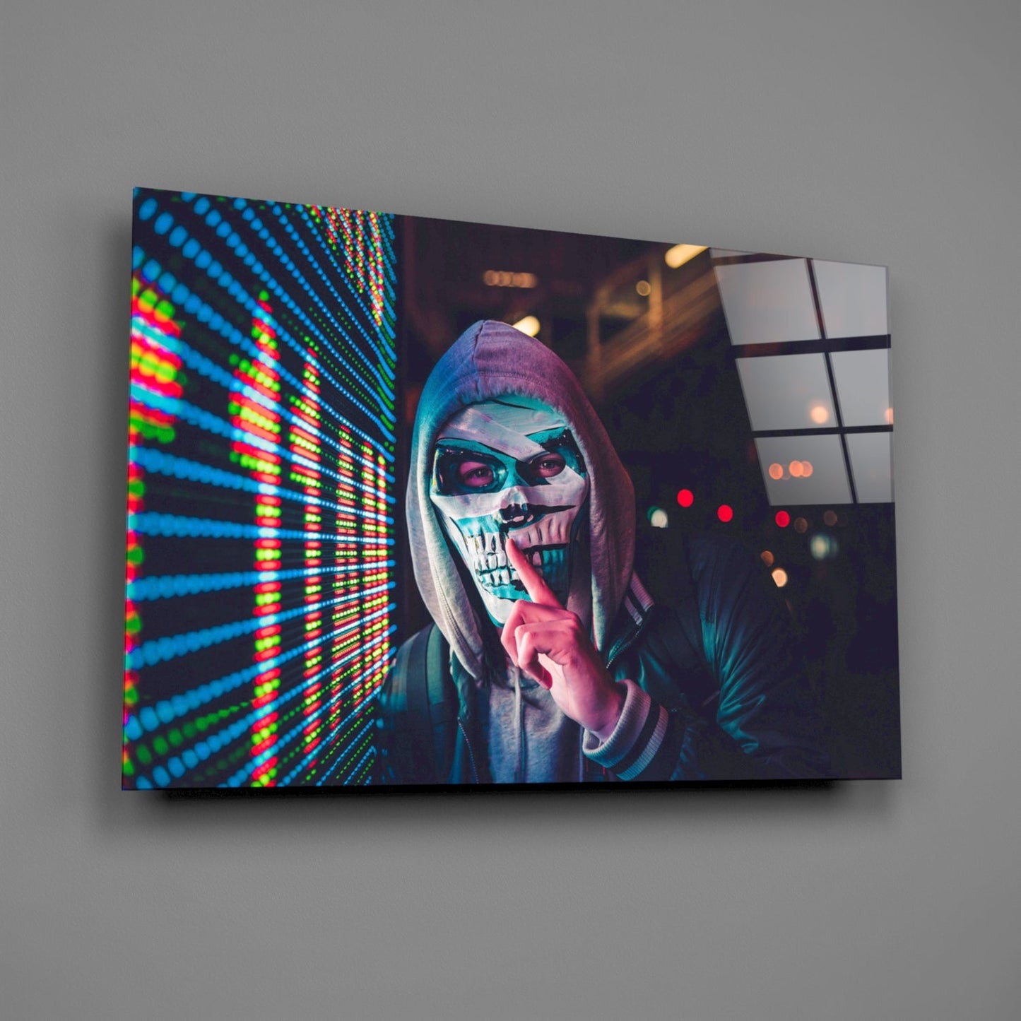 Angled view of glass wall art featuring a skull-masked figure in hoodie with neon blue and green LED display on left side, mounted on gray wall.
