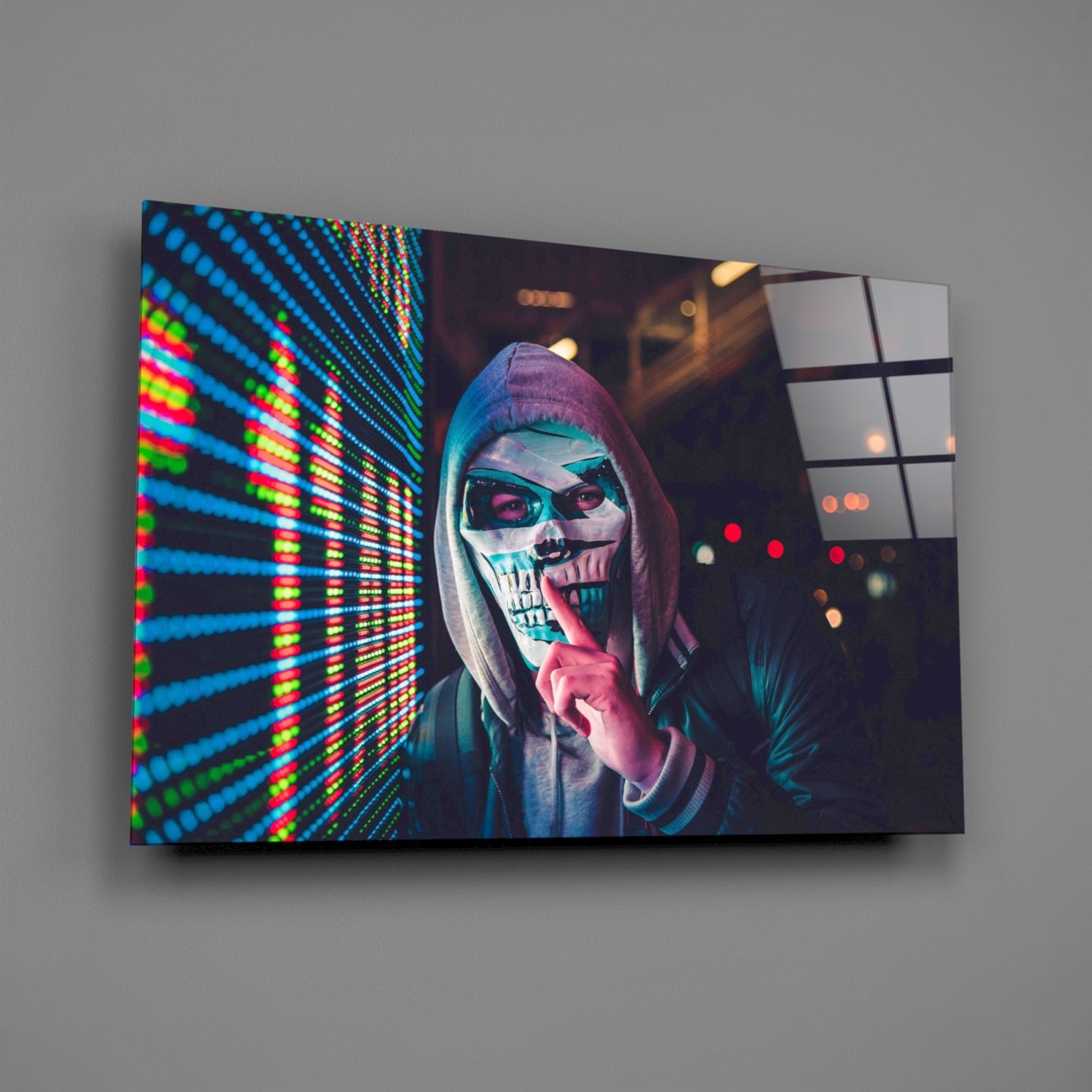 Angled view of glass wall art featuring a skull-masked figure in hoodie with neon blue and green LED display on left side, mounted on gray wall.
