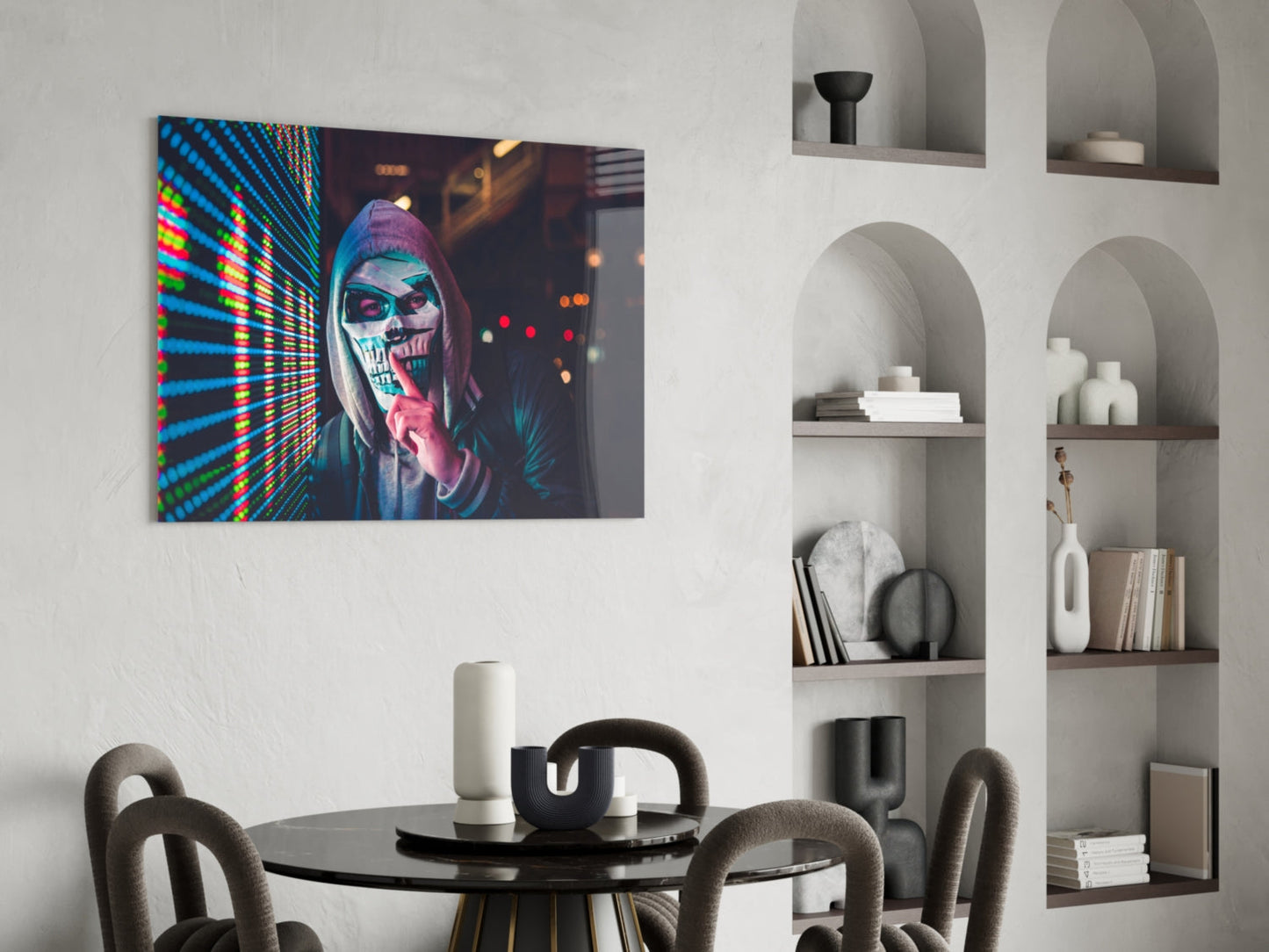 Neon skull artwork displayed on white wall above black round dining table with gray chairs and white shelving unit.