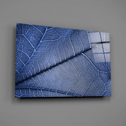 Blue glass wall art displaying detailed leaf vein patterns in deep blue and white tones, mounted at an angle against a gray wall.
