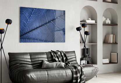 Blue glass wall art displaying detailed leaf vein texture mounted above black leather sofa in modern living room setting.