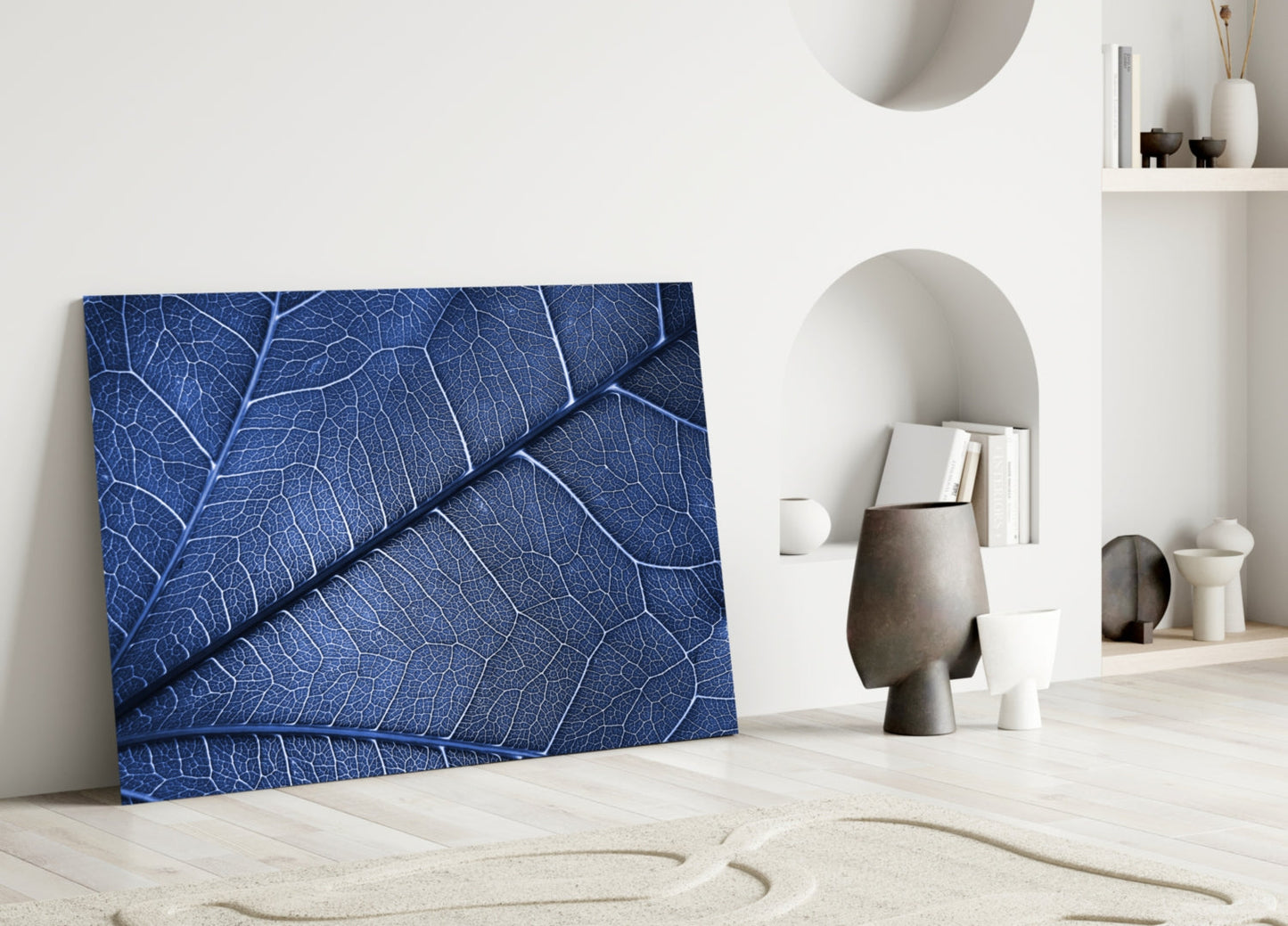 Blue glass wall art with detailed leaf vein texture displayed against white wall beside decorative objects.
