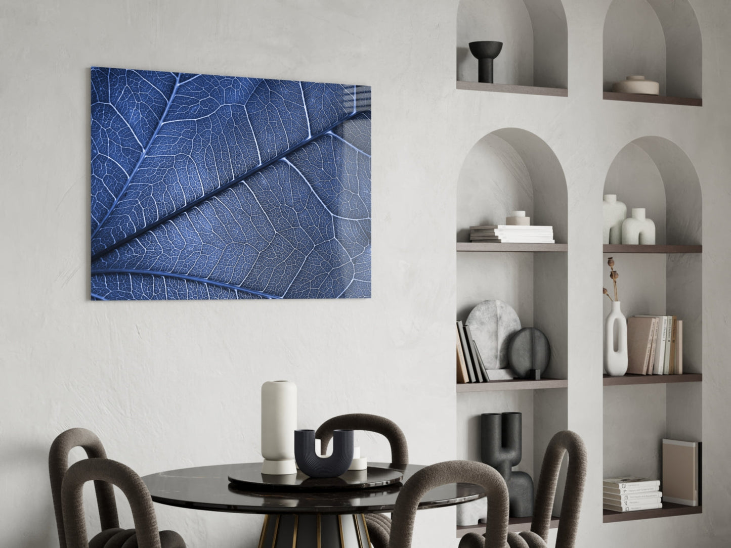 Blue leaf vein pattern glass wall art displayed above black round dining table with gray upholstered chairs.
