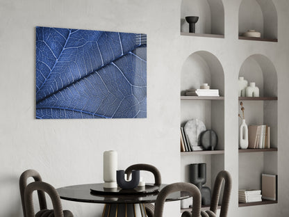 Blue leaf vein pattern glass wall art displayed above black round dining table with gray upholstered chairs.