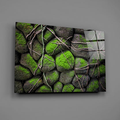 Glass wall art displaying moss-covered gray stones with tan vine tendrils, mounted on gray wall at angle.