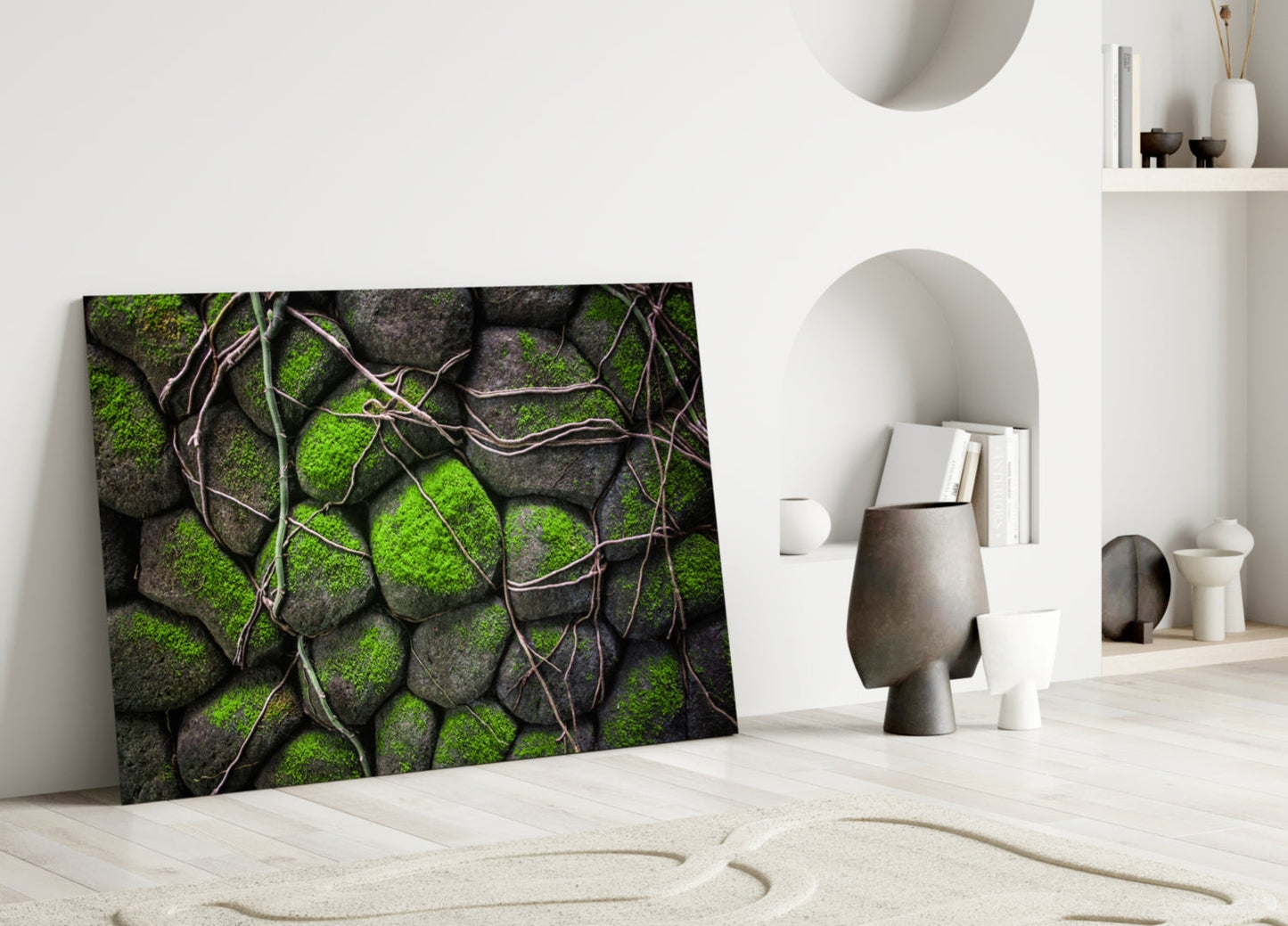 Mossy Stones glass wall art leaning against white wall in minimalist interior with decorative objects and shelving.