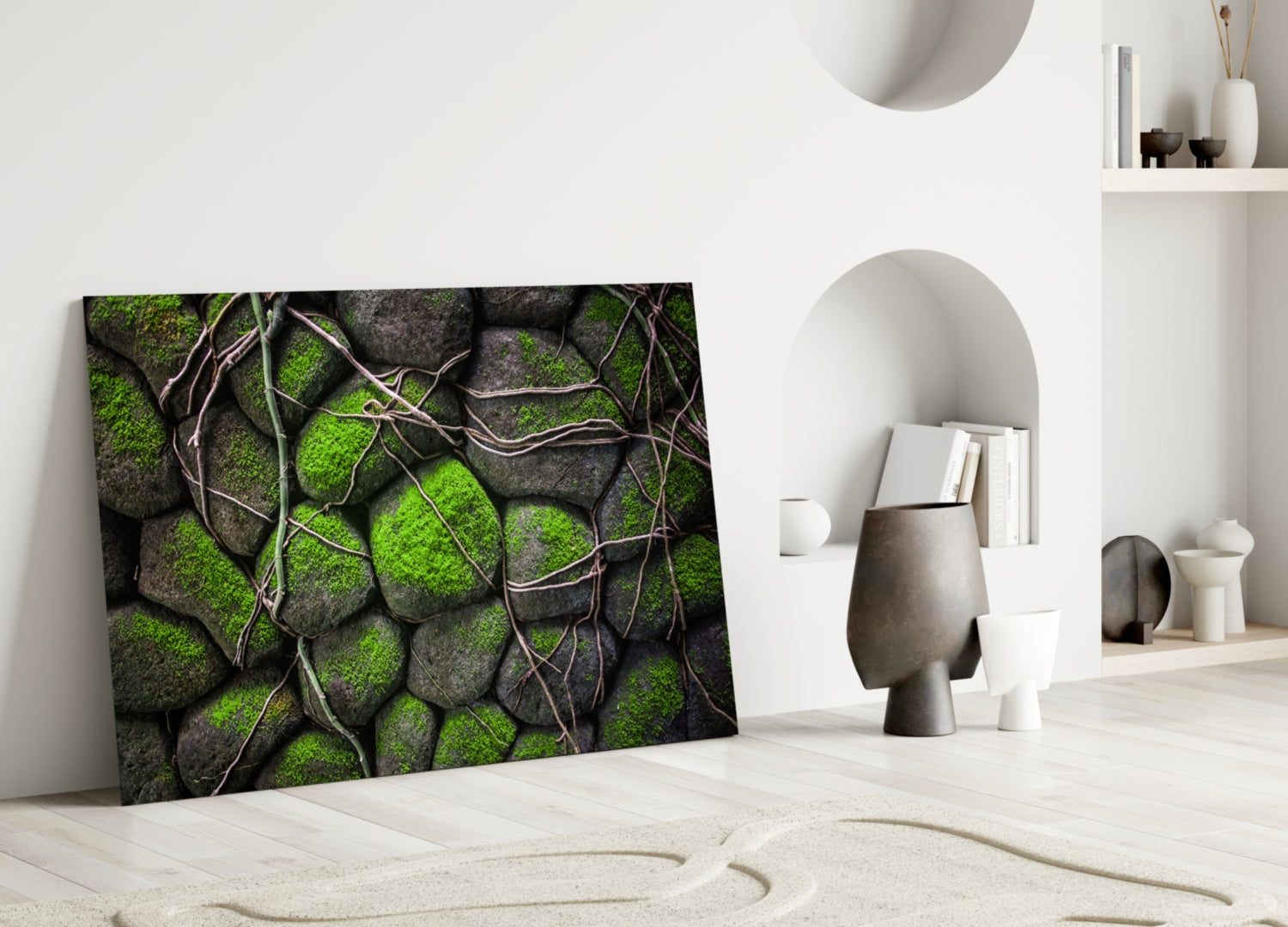 Mossy Stones glass wall art leaning against white wall in minimalist interior with decorative objects and shelving.