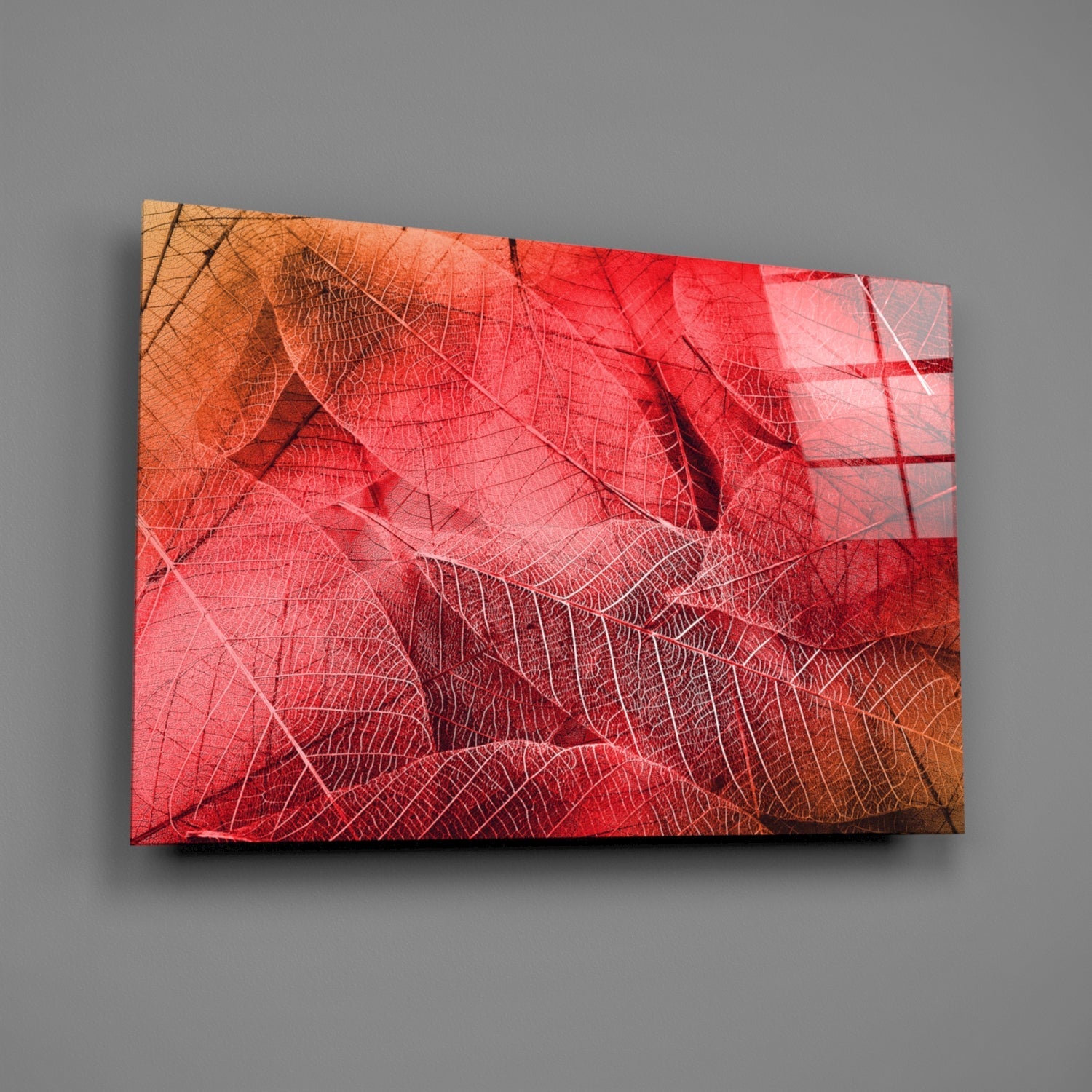 Angled view of glass wall art displaying overlapping red and orange autumn leaves with detailed vein patterns against a gray background.
