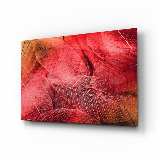 Angled perspective of a glass wall art panel displaying layered red and orange autumn leaves with detailed vein patterns, mounted against a white background.