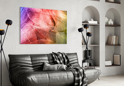 Colorful macro leaf glass art in pink, orange, and yellow tones displayed above black leather sofa in modern living room.