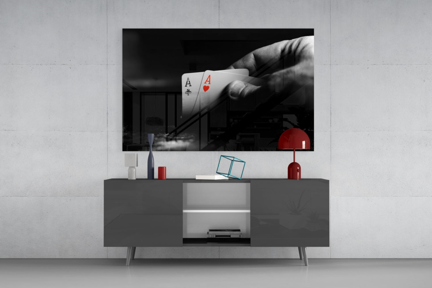 Black and white glass wall art displaying a hand holding two aces above a modern gray media console with red accents.