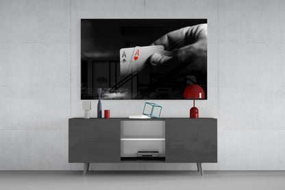 Black and white glass wall art displaying a hand holding two aces above a modern gray media console with red accents.