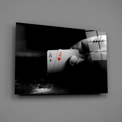 Black and white photograph of a hand holding two playing cards—an Ace of Clubs and Ace of Hearts with red suit symbol—mounted as glass wall art.