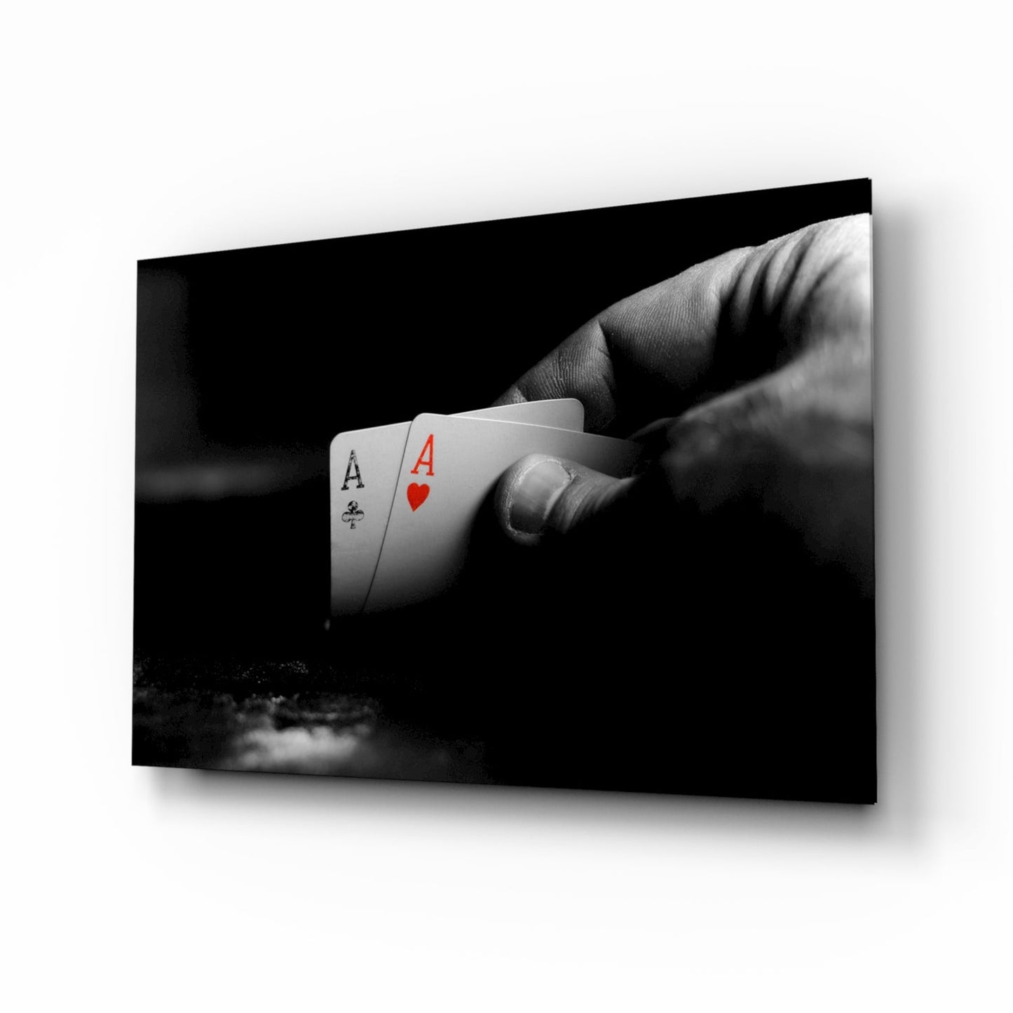 Black and white photograph of a hand holding two playing cards—Ace of Clubs and Ace of Hearts—displayed on glass wall art.