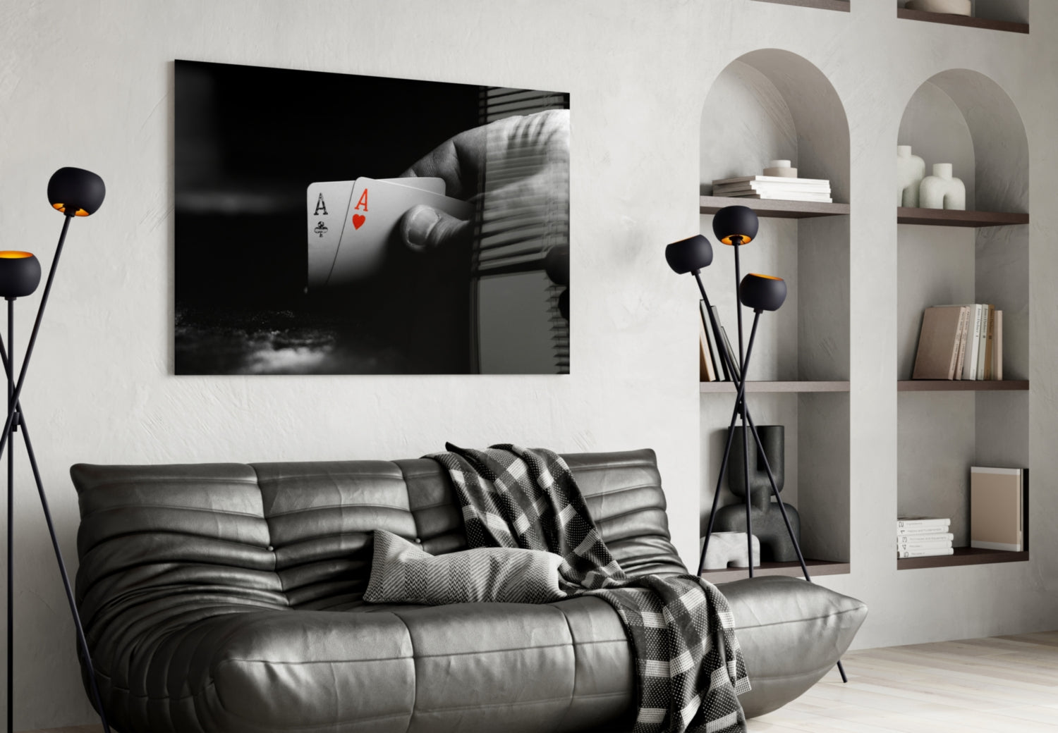 Black and white glass wall art depicting a hand holding two aces playing cards displayed above a gray leather sofa in a modern living room.