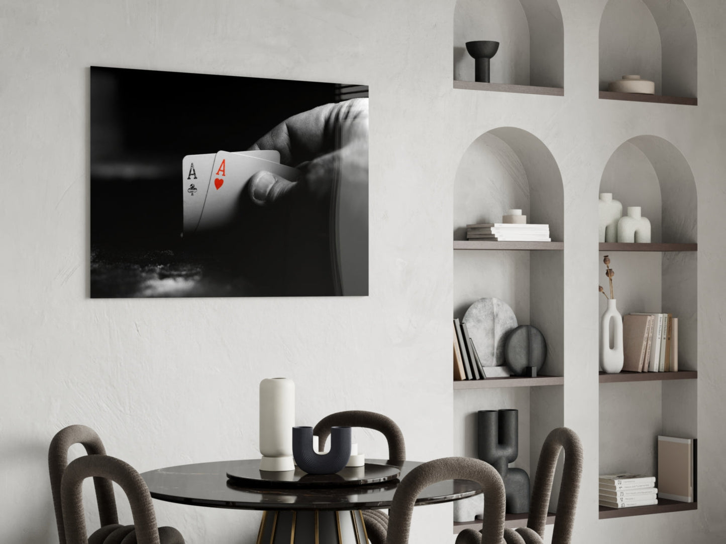 Black and white glass wall art displaying a hand holding two aces playing cards mounted above a round black dining table.