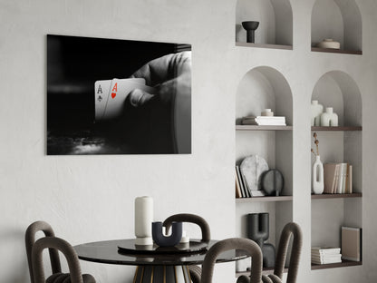 Black and white glass wall art displaying a hand holding two aces playing cards mounted above a round black dining table.