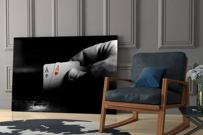 Black and white glass wall art displaying a hand holding two playing cards—ace of spades and ace of hearts—mounted in modern living room setting.