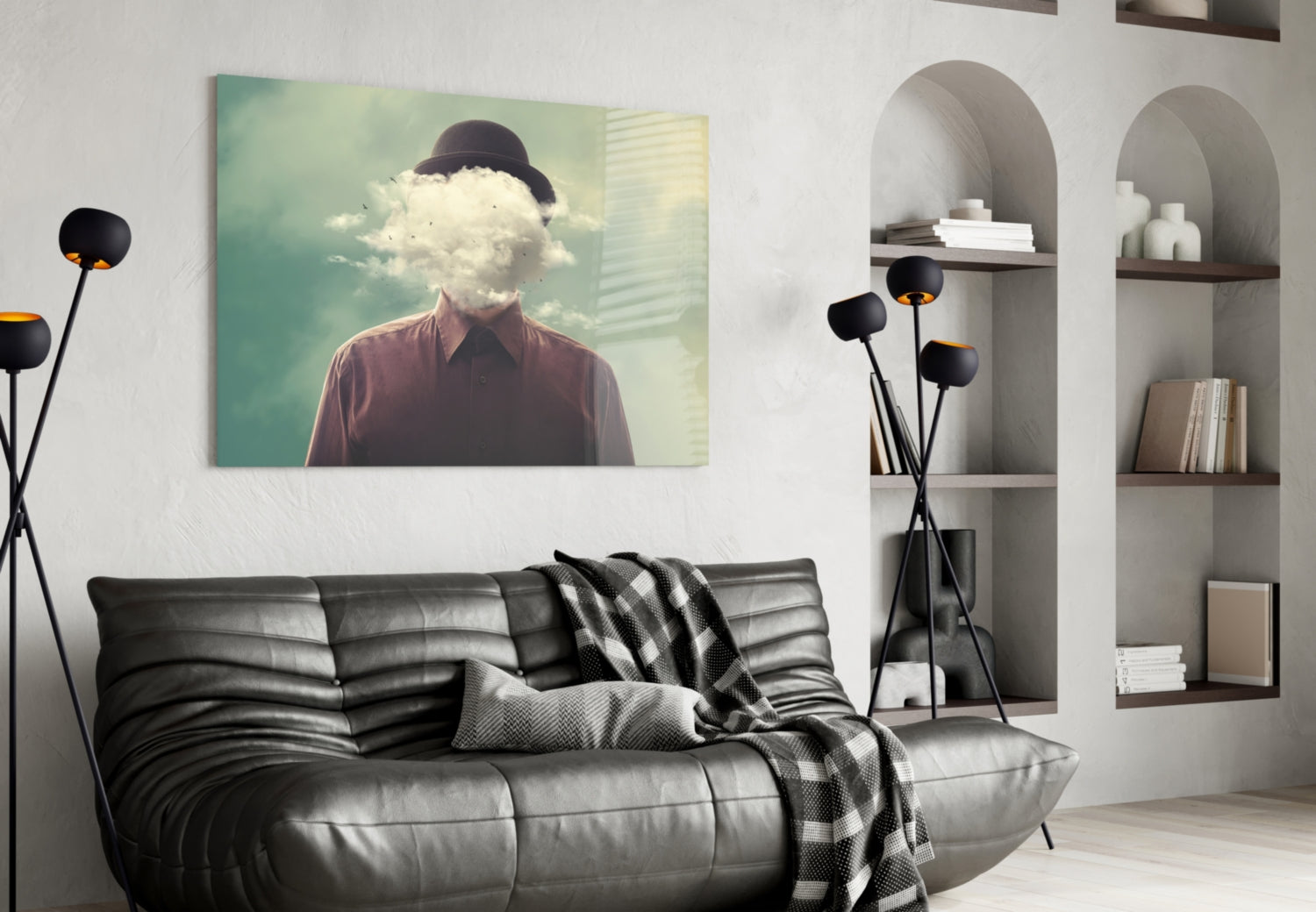 Surreal glass wall art depicting a man with bowler hat and cloud replacing his head, displayed above black leather sofa in modern living room setting.