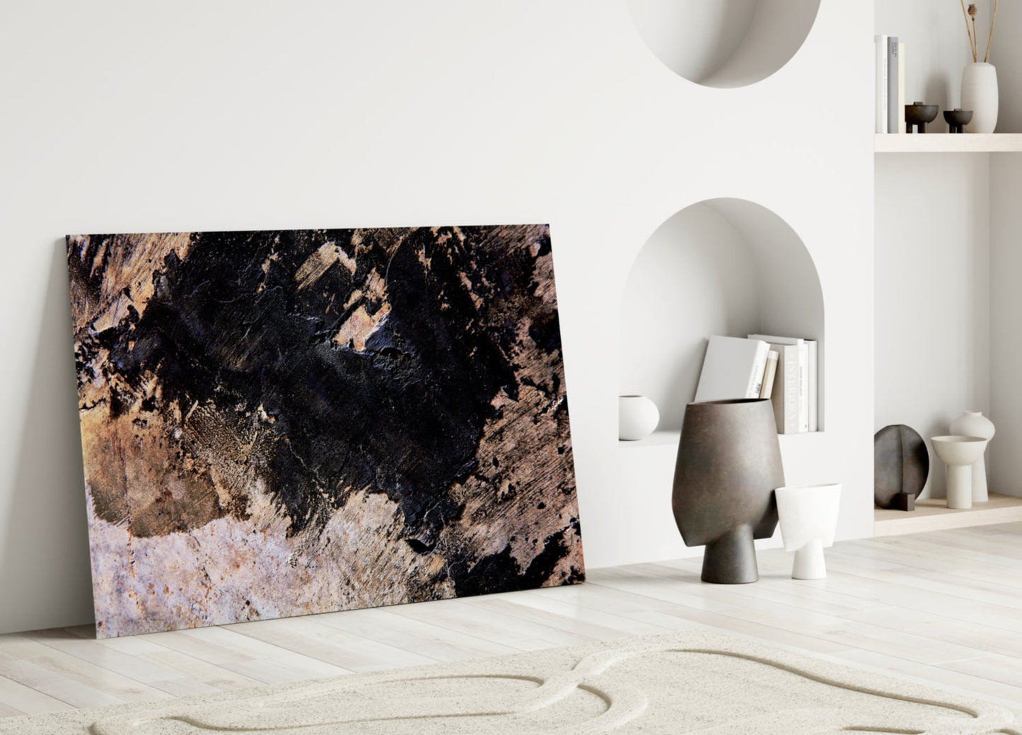 Abstract glass wall art with black, tan, and rust textured patterns leaning against white interior wall with decorative objects.