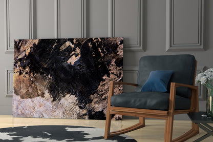 Glass wall art featuring black, tan, and white abstract textured pattern displayed in modern living room with wooden rocking chair and blue pillow.