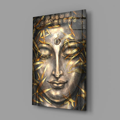 Glass wall art featuring a serene Buddha face with closed eyes, gold leaf accents, and ornamental spiral details, displayed at an angle against gray background.