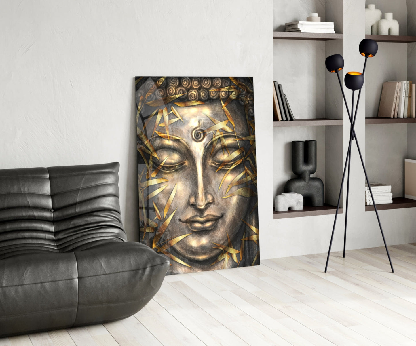Gold and gray Buddha face glass wall art displayed in modern living room with black leather chair and shelving.