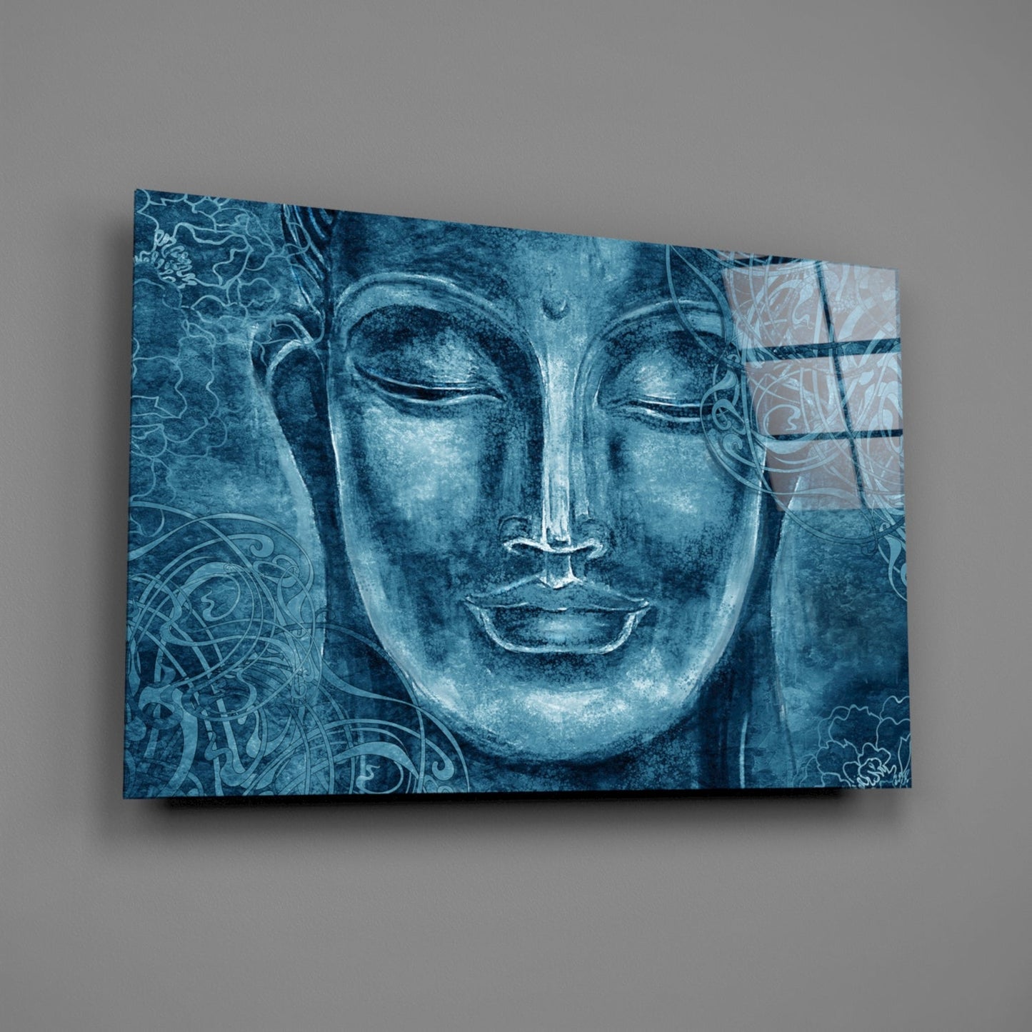 Blue-toned glass wall art featuring a serene Buddha face with ornamental patterns, displayed at an angle against a gray background.