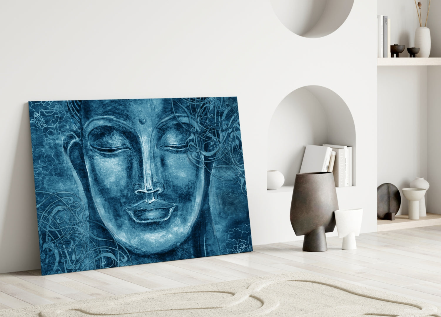 Blue glass wall art depicting a serene Buddha face with ornamental patterns, leaning against white wall in minimalist room setting.