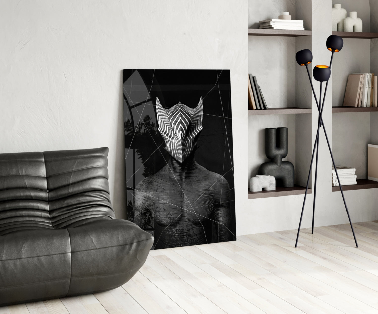 Black and white glass wall art depicting an abstract figure with geometric patterns displayed in a modern living room with gray leather furniture and shelving.