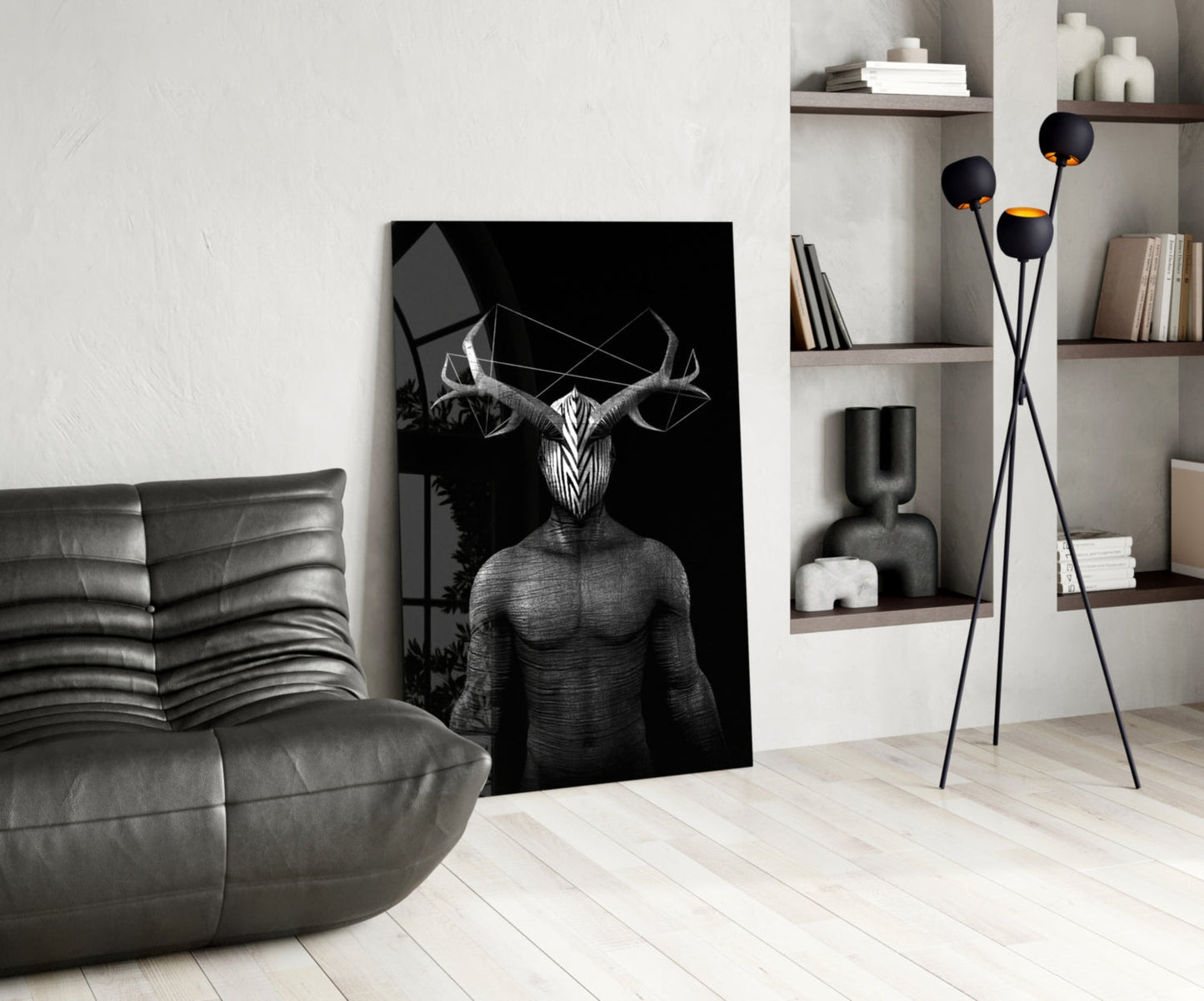 Black and white glass wall art depicting a surreal humanoid figure with large horns, displayed in a modern living room with gray leather furniture and wooden shelving.