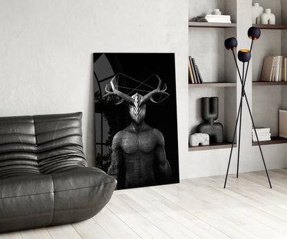 Black and white glass wall art depicting a surreal humanoid figure with large horns, displayed in a modern living room with gray leather furniture and wooden shelving.