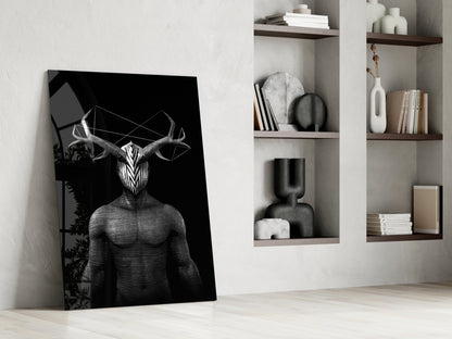 Black and white glass art depicting surreal horned figure leaning against white wall near shelving unit with books and decorative objects.