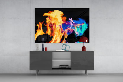 Vibrant glass wall art displaying abstract flames in yellow, orange, and blue mounted above a gray media console in a modern living room setting.