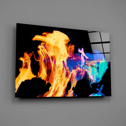 Angled view of glass wall art displaying vibrant orange flames on left transitioning to colorful abstract forms in blue, purple, and teal on right side.