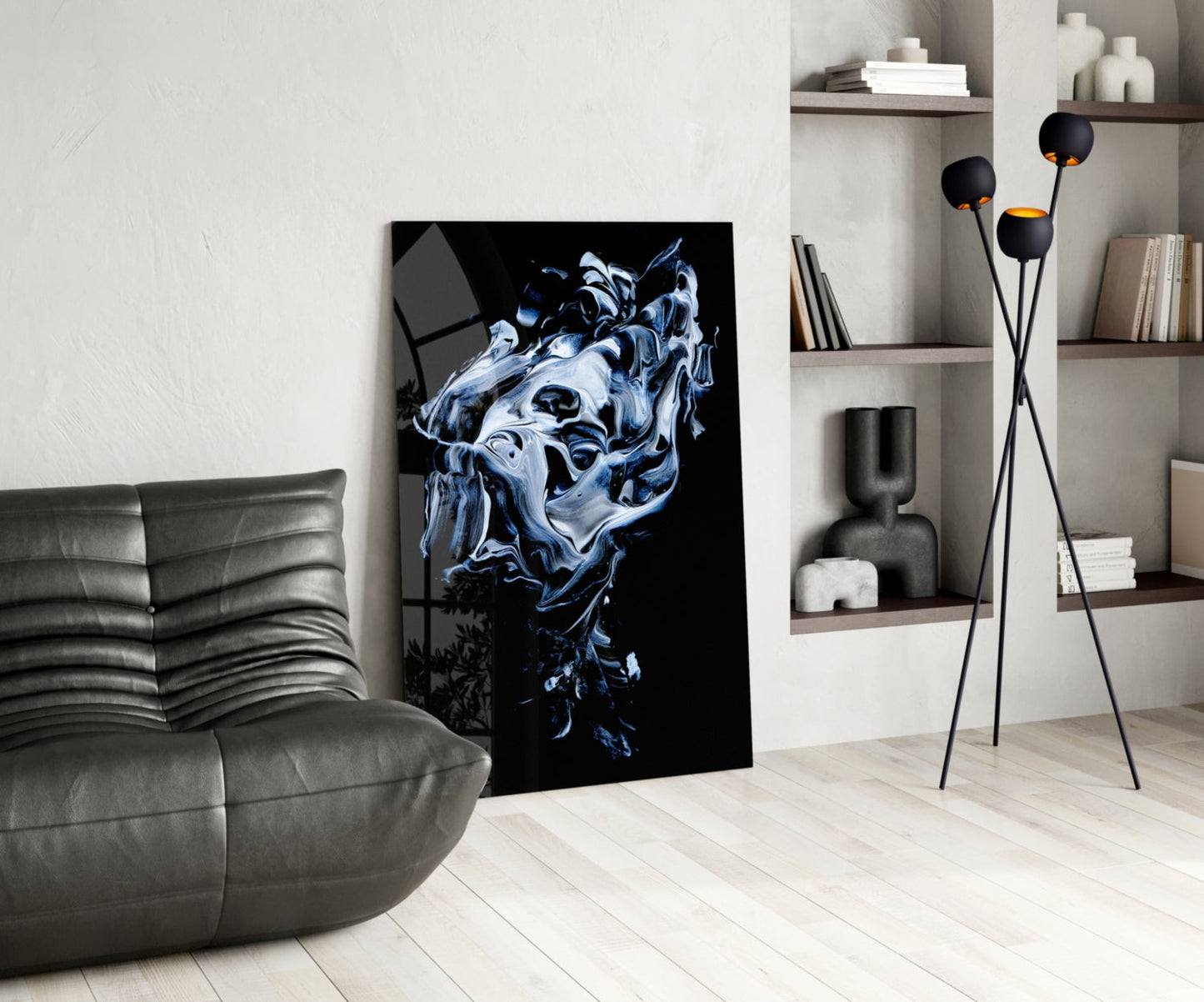 Abstract gray and blue glass wall art depicting a liquid face form displayed in a modern living room with gray sofa and shelving.