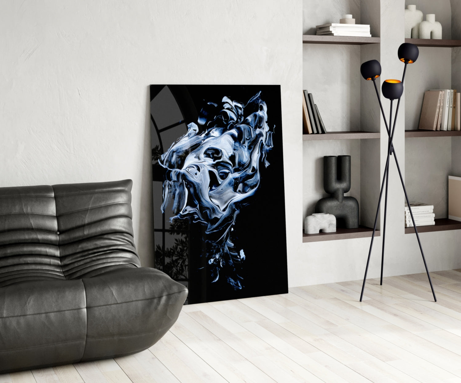 Abstract gray and blue glass wall art depicting a liquid face form displayed in a modern living room with gray sofa and shelving.