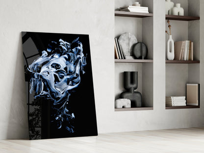 Abstract gray glass wall art leaning against white wall beside shelving unit displaying books and decorative objects.