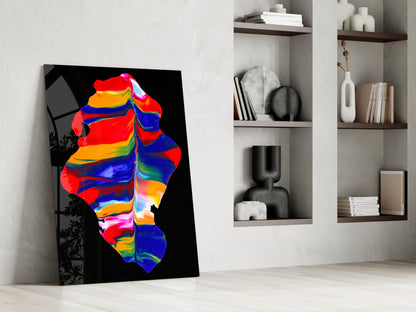 Colorful thermal art glass leaning against white wall beside shelving unit holding books and decorative objects.