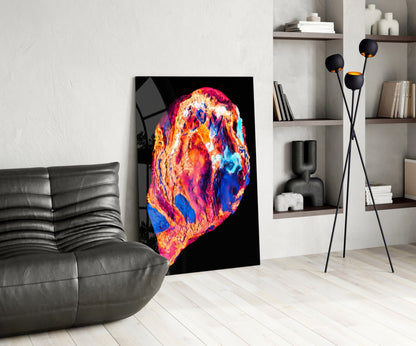 Colorful lava glass wall art with vibrant orange, red, pink, blue, and yellow swirls displayed in a modern living room next to a gray leather chair.