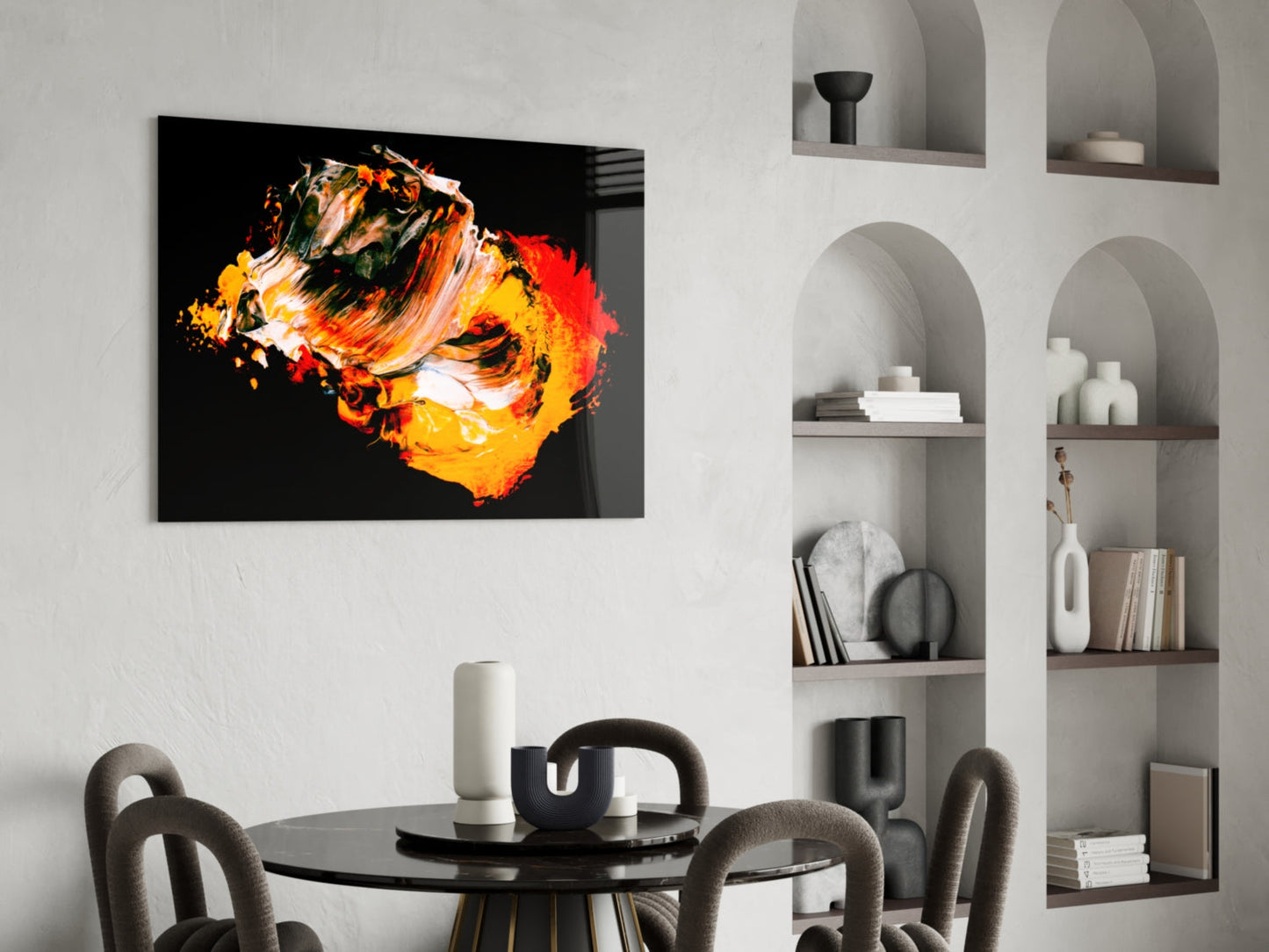 Abstract glass wall art with orange, yellow, and red brushstrokes on black background, displayed above dining table in modern interior.