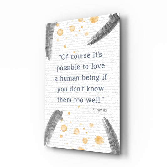 Angled 3D view of glass wall art displaying Bukowski quote in blue text with gray brush strokes and gold watercolor dots on white textured background.