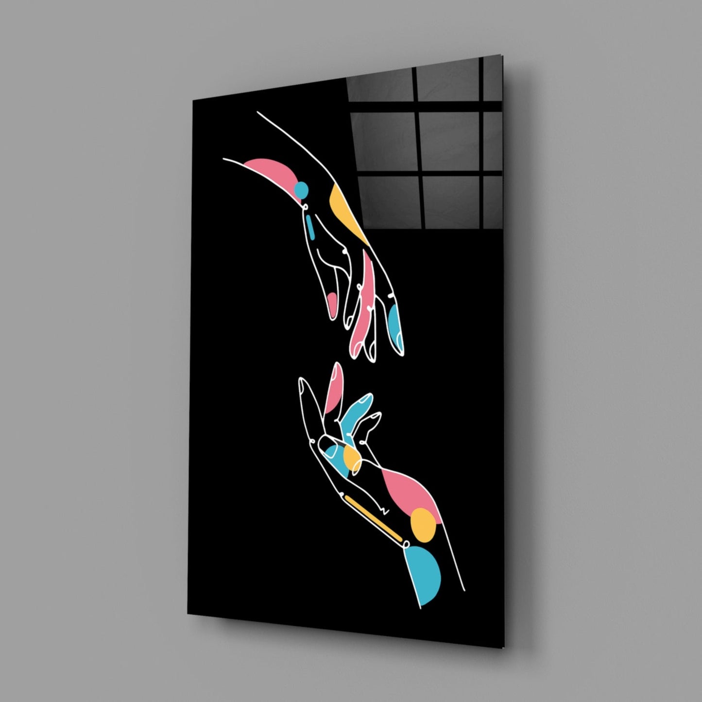Black glass panel with two outlined hands in white holding colorful geometric shapes in pink, blue, and yellow, displayed at an angle against gray wall.