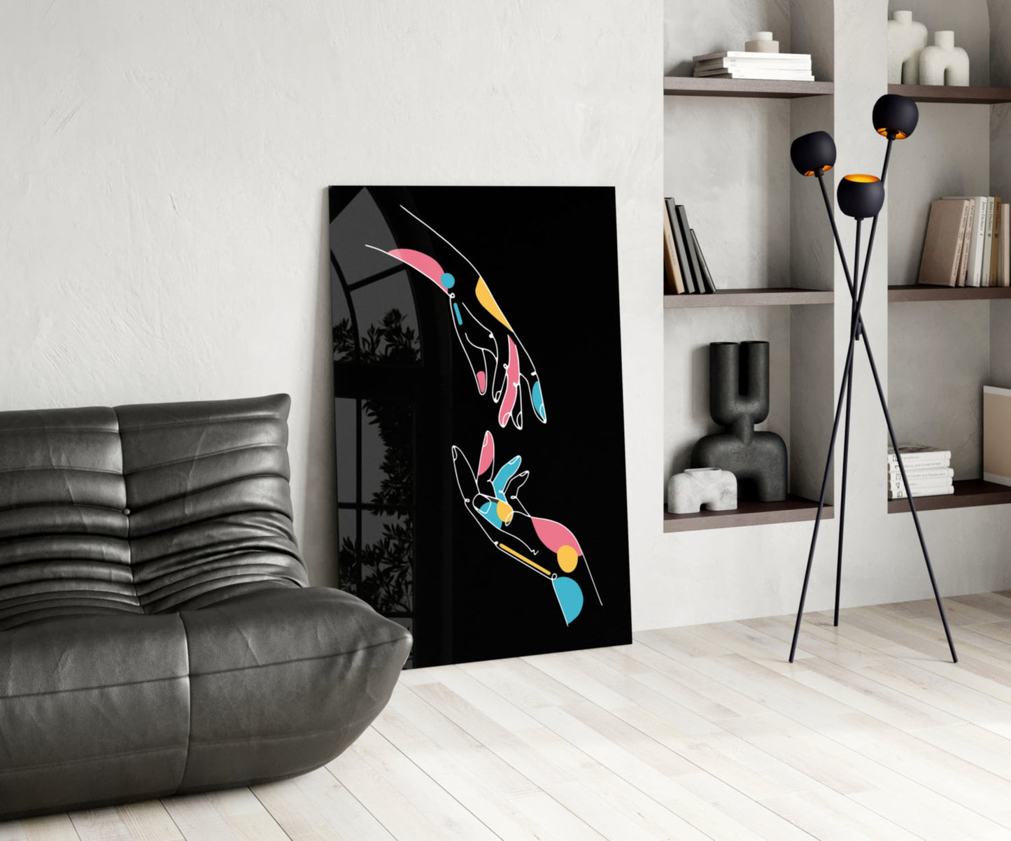 Modern living room interior featuring abstract glass wall art with colorful neon hands on black background, displayed next to gray sofa and white shelving unit.