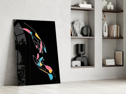 Abstract colorful hands glass wall art leaning against white wall beside shelving unit displaying books and decorative objects.