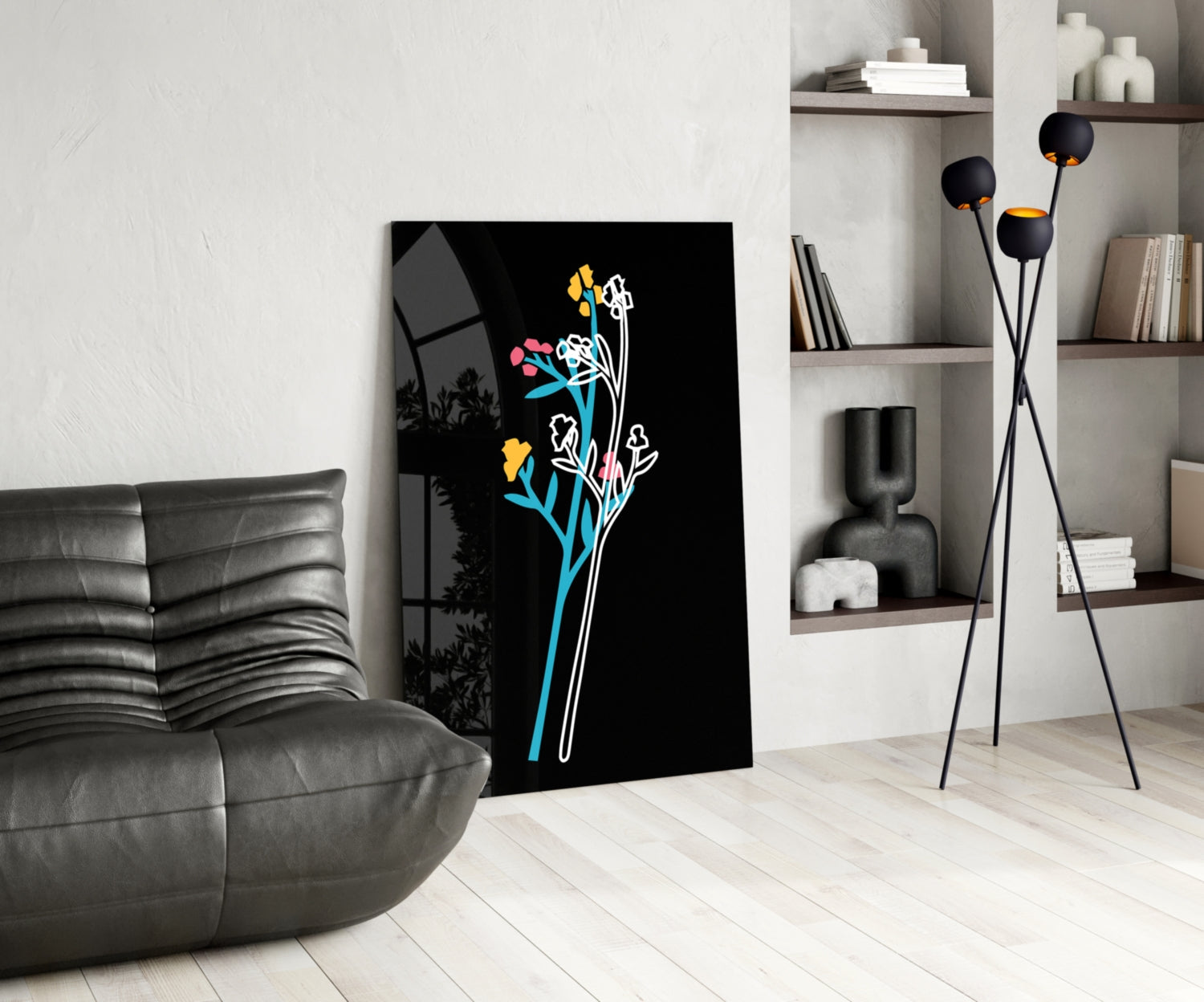Modern living room interior with black glass wall art displaying colorful neon flowers in blue, yellow, and pink against white shelving and gray leather sofa.